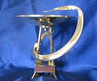 a serpent curls a bowl atop a tower, made of gold metal.