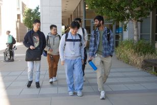 Five students walking outside campus building and smiling.