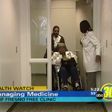 a patient in a wheelchair is pushed by another person while a health care provider holds a door open
