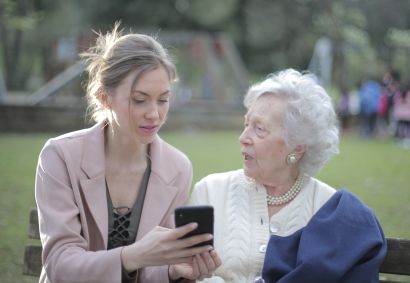on a park bench a young woman shows an older woman a cellphone.
