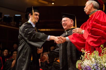 graduate receives diploma with handshake from the dean