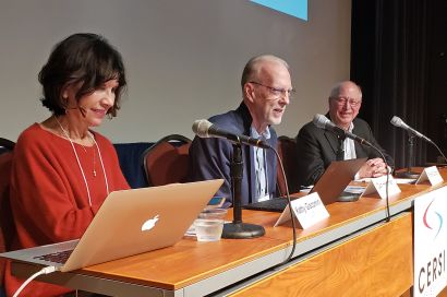 Giacomini, Hartman, and Gupton sit in front of microphones on a conference stage