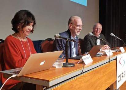 Giacomini, Hartman, and Gupton sit in front of microphones on a conference stage