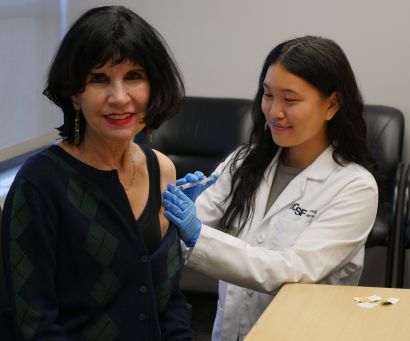 Pharmacy student in white coat administers flu shot to dean