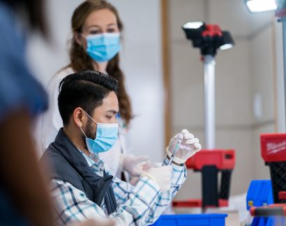 A man wearing a mask measures vaccine in a syringe.
