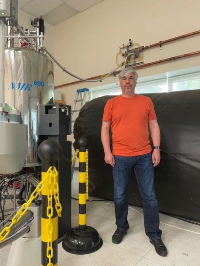 Kelly stands next to an NMR machine and helium collection bag