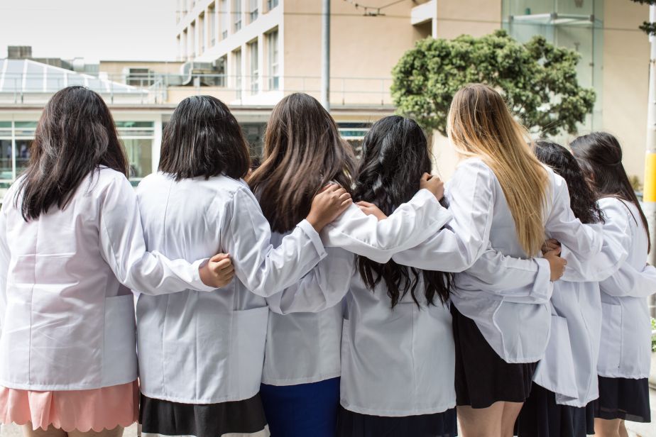 7 students in white coats arm in arm.