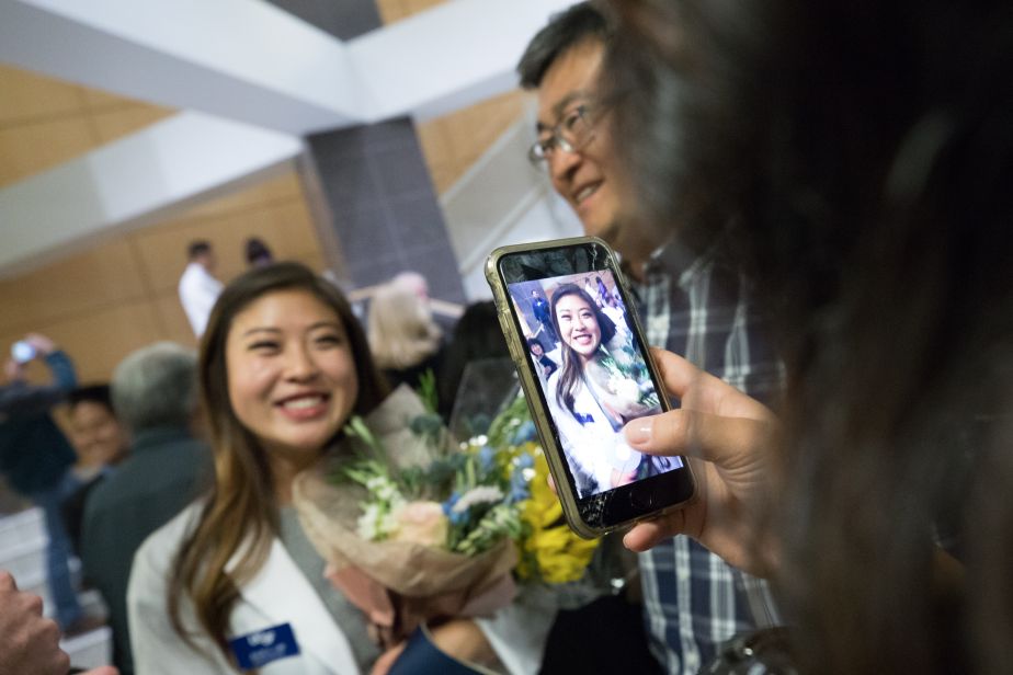 A cellphone captures a smiling student holding a bouquet.