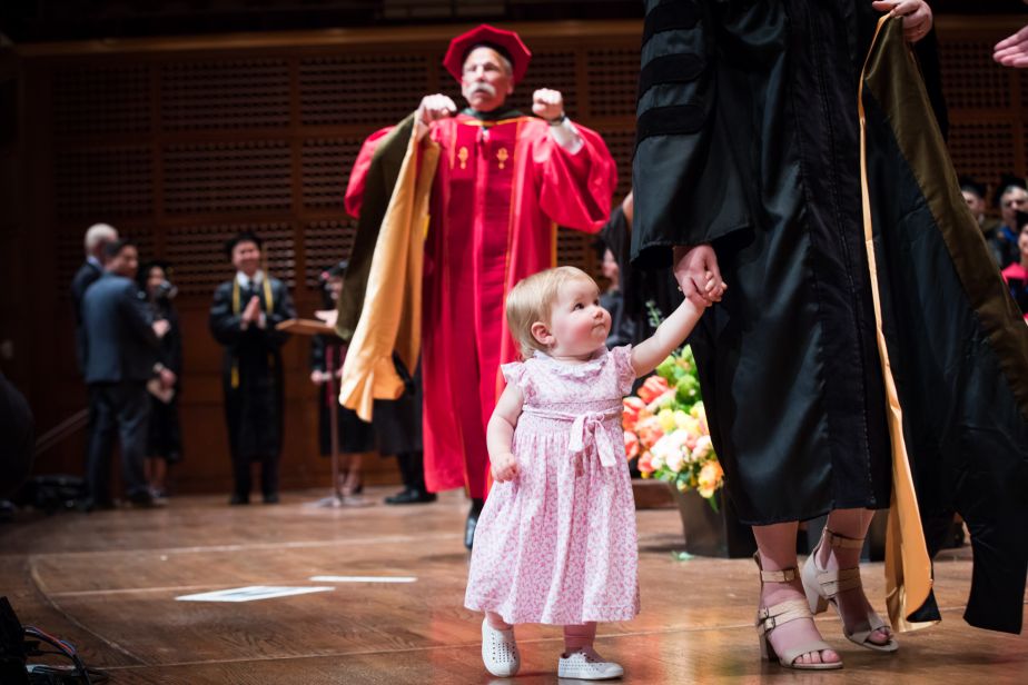 a graduate and her toddler walk across the stage together.
