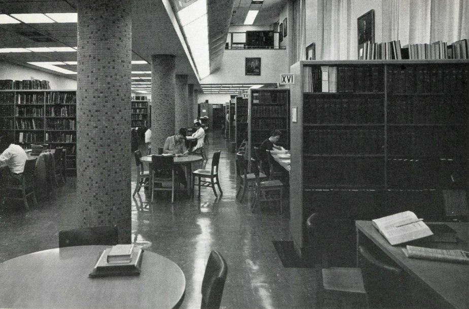 seated people working at tables surrounded by library stacks.