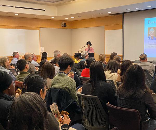 people in audience listen to a speaker at a podium in a crowded room