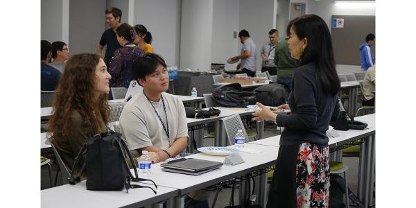Two AICD3 students seated with Joanna Chun standing in classroom