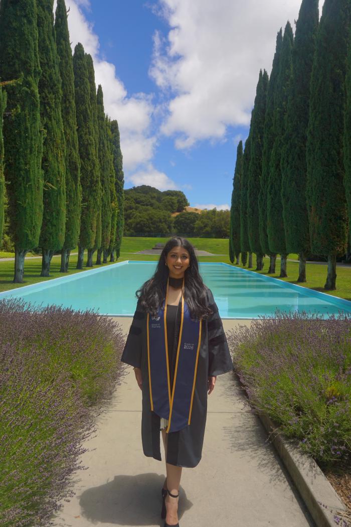 Rhea Misra in commencement attire with landscape background